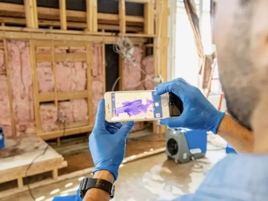 Technician scanning open wall framing with a thermal camera to map hidden moisture during a dry-out