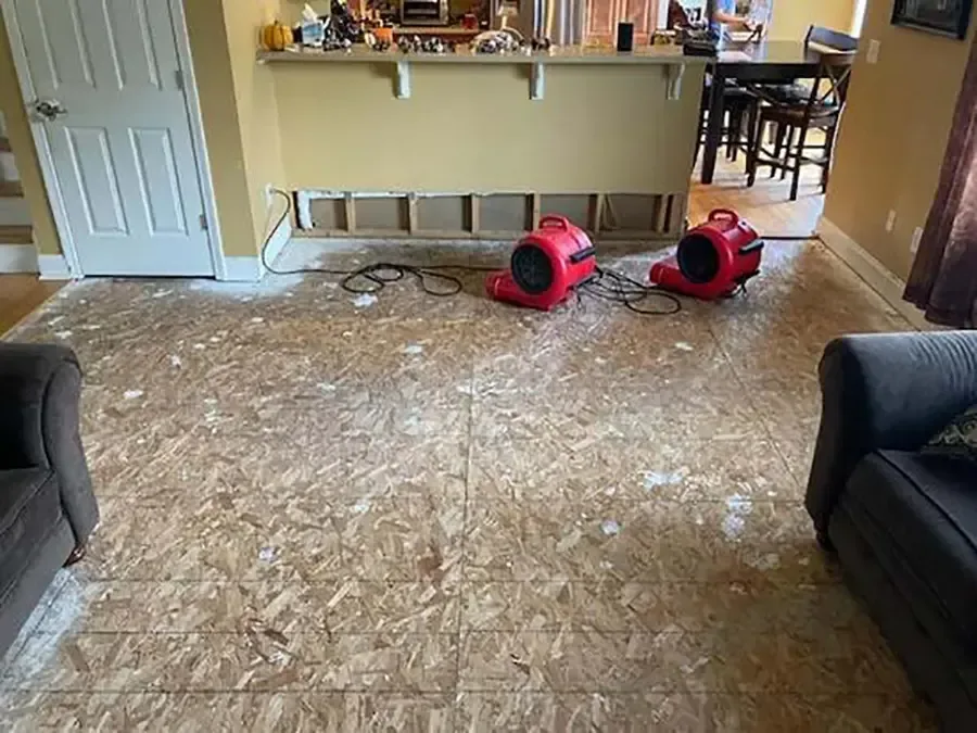 Red air movers drying an exposed subfloor in a living room after the flooring came up
