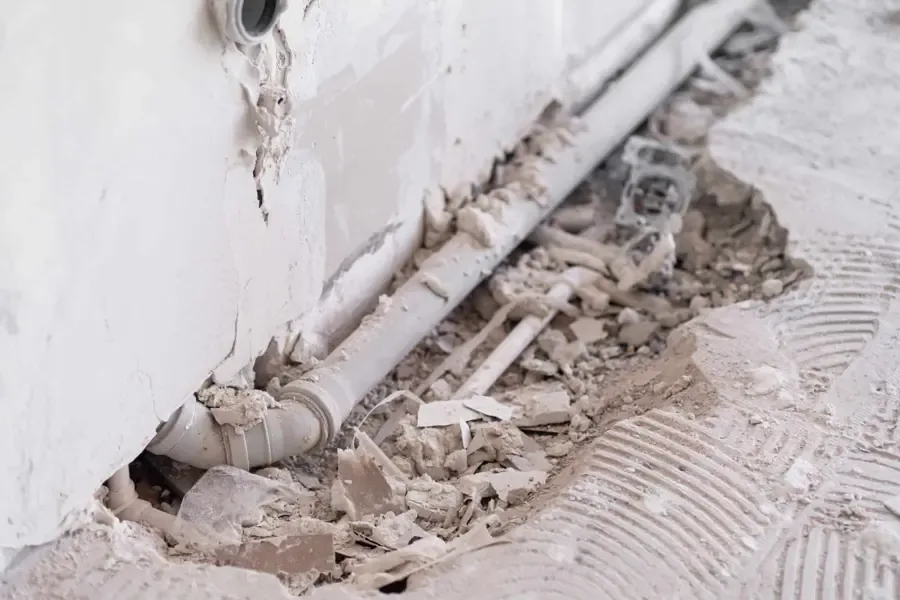 Tile and mortar chipped out of a concrete slab to expose a leaking water pipe